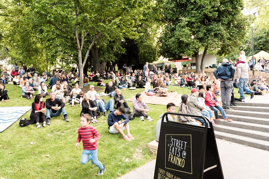 A crowd sitting on the lawn under trees at Street Eats Franko